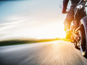 motorcyclist riding on highway towards the sun